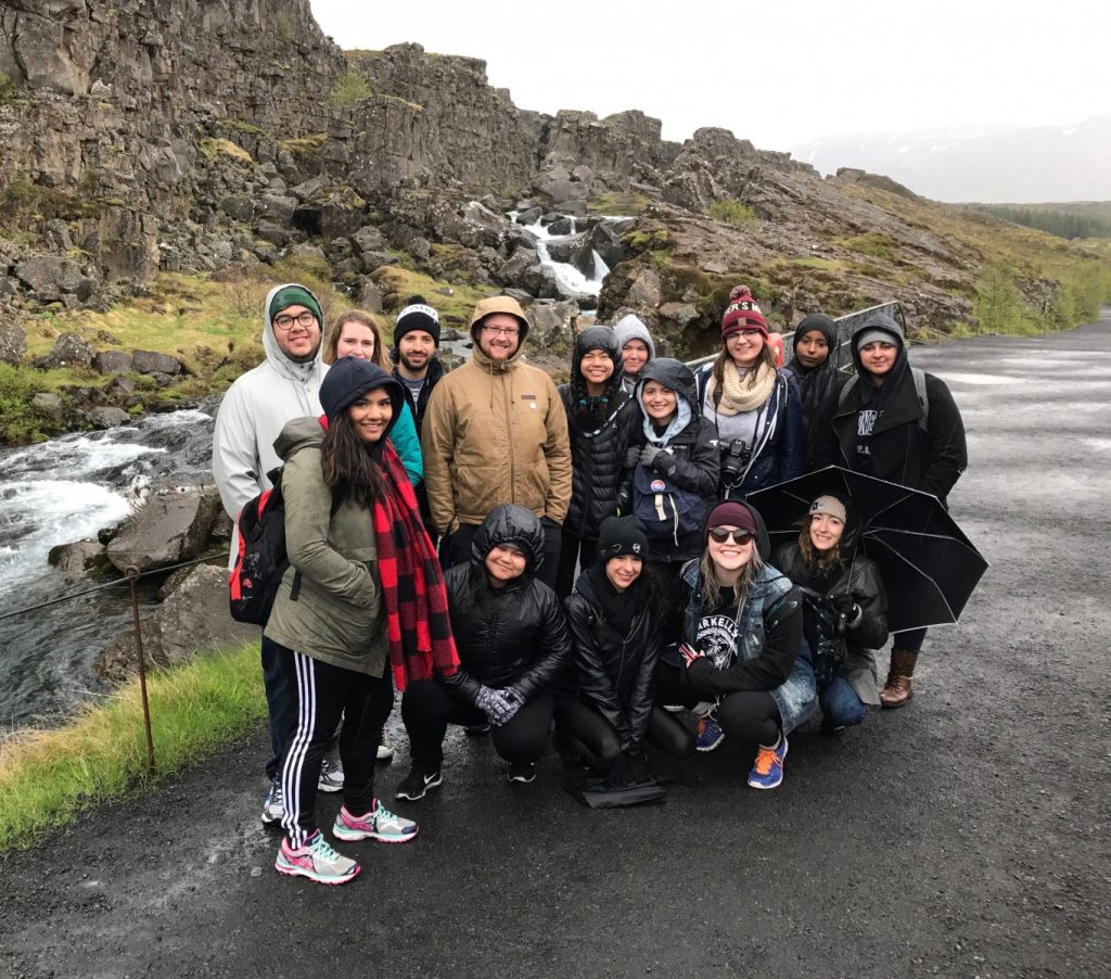 Group of students dressed in rain gear pose in front of a green cliffy landscape