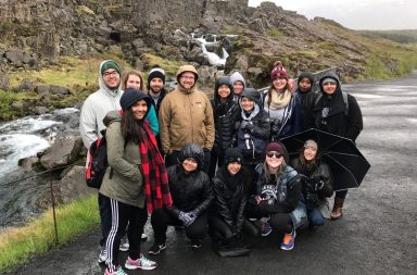 Group of students dressed in rain gear pose in front of a green cliffy landscape