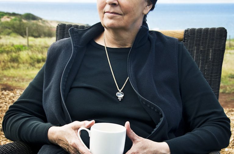 A woman wearing a necklace sitting on a chair having a tea or coffee.
