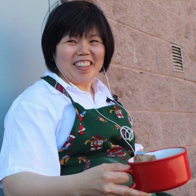 woman smiling and wearing an apron and holding onto her lunch container during her break