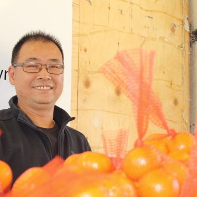 man smiling with oranges in red bags