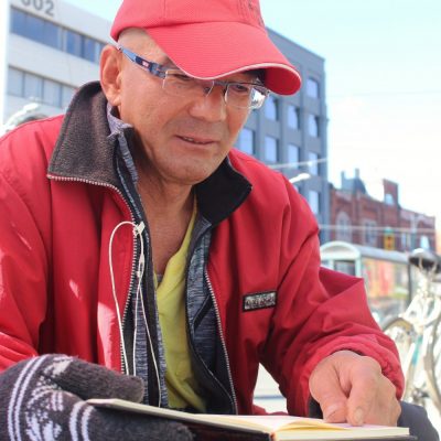 man in hat looking at book on the street of Chinatown